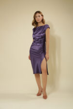 ZUMO FASHION satenska haljina rađena po meri sa blago prekrivenim ramenima, naborima koji oblikuju figuru i dubokim šlicem iznad kolena. Dostupna u četiri dužine, savršena je za svečane prilike i letnje proslave.